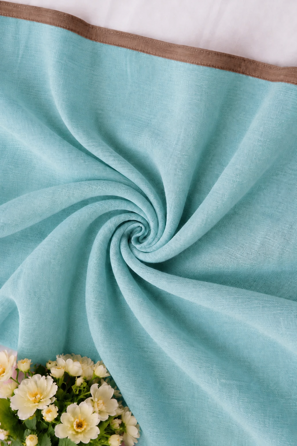 A close-up of a light aqua blue fabric, likely a scarf or throw, styled in a spiral drape with a brown border and white flowers at the bottom left.