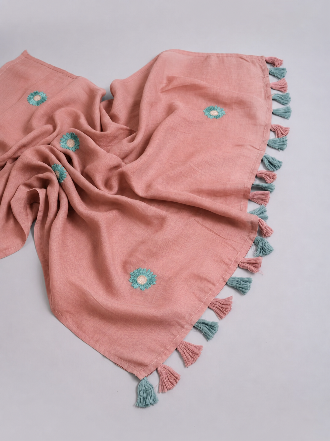 Close-up of a blush pink mul cotton pallu with aqua daisy embroidery and blush-and-aqua tassels.