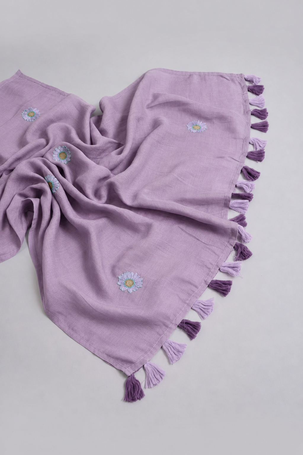 Mauve mul cotton saree pallu with lavender daisy embroidery and lavender-and-purple tassels.