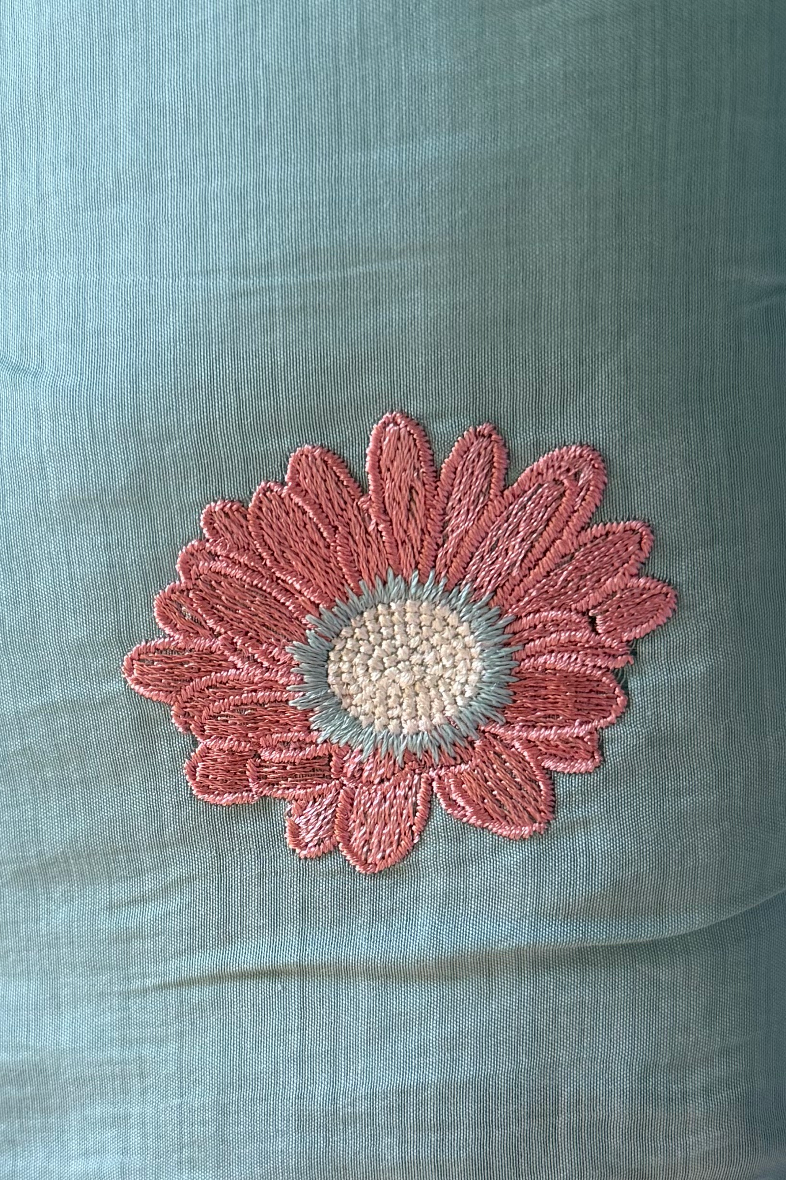 Macro of a single dusty-rose daisy embroidered in viscose thread on aqua mul cotton.