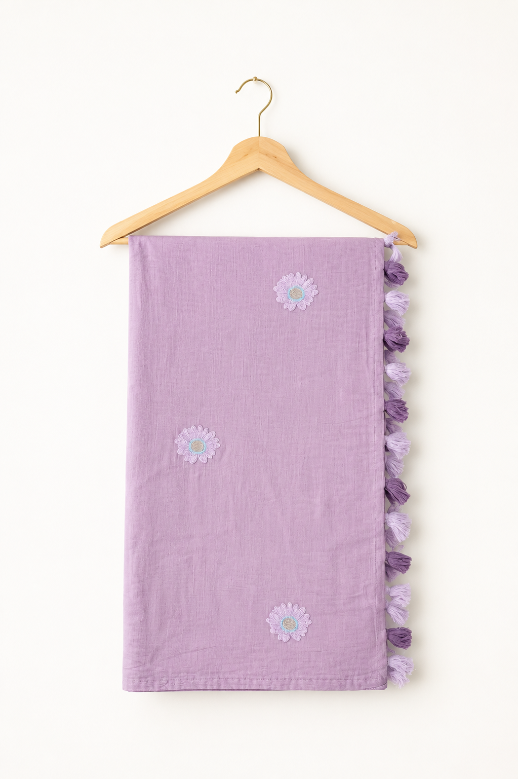 Mauve mul cotton saree with lavender daisy embroidery and lavender-and-purple tassels, folded on a hanger.