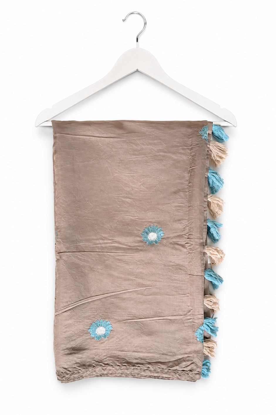 A taupe-brown cotton scarf with blue and beige tassels and embroidered flowers, hanging on a white wooden hanger against a white background.