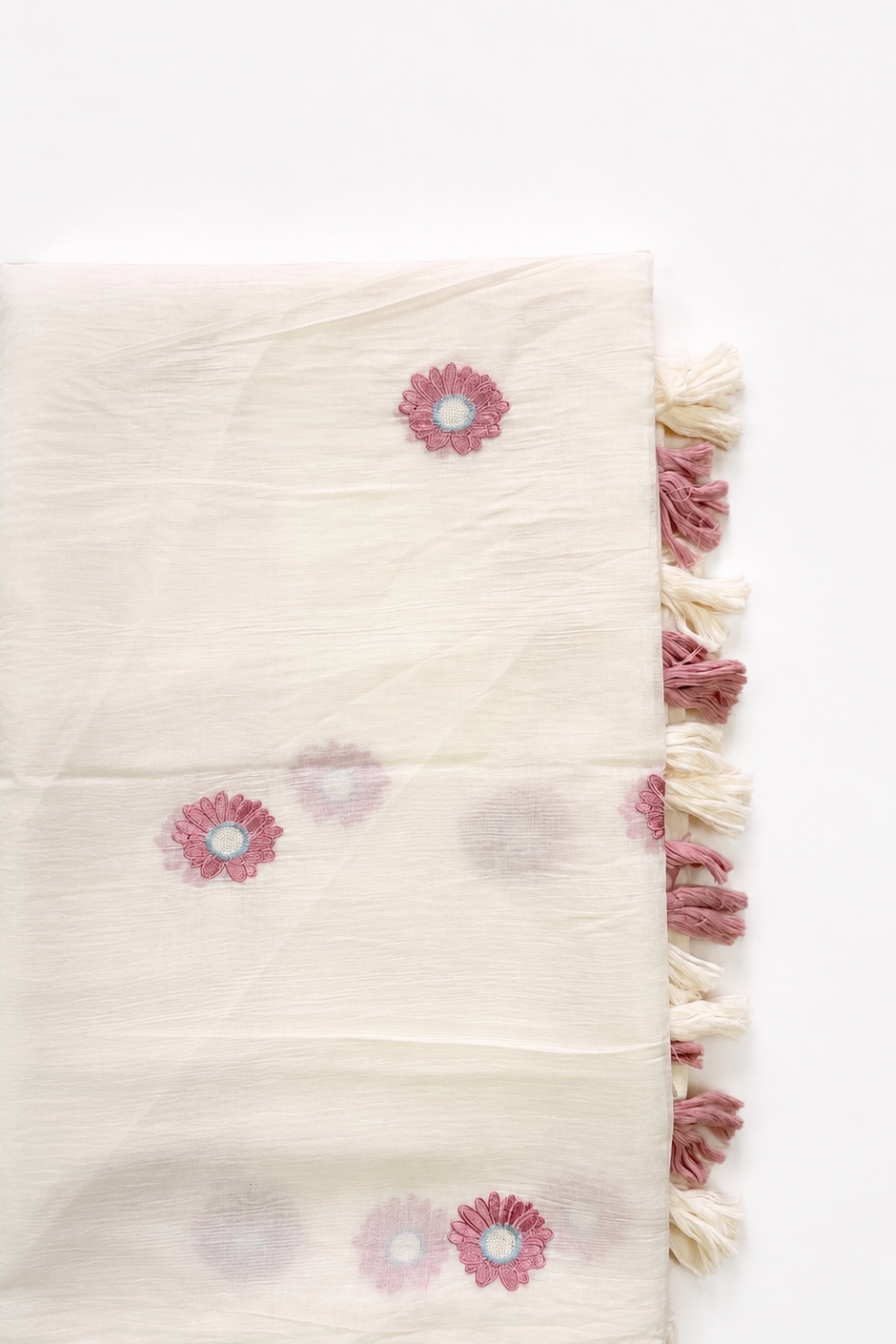 Folded ivory mul cotton saree showing scattered dusty-rose daisy motifs and cream-and-rose tassels along the edge.