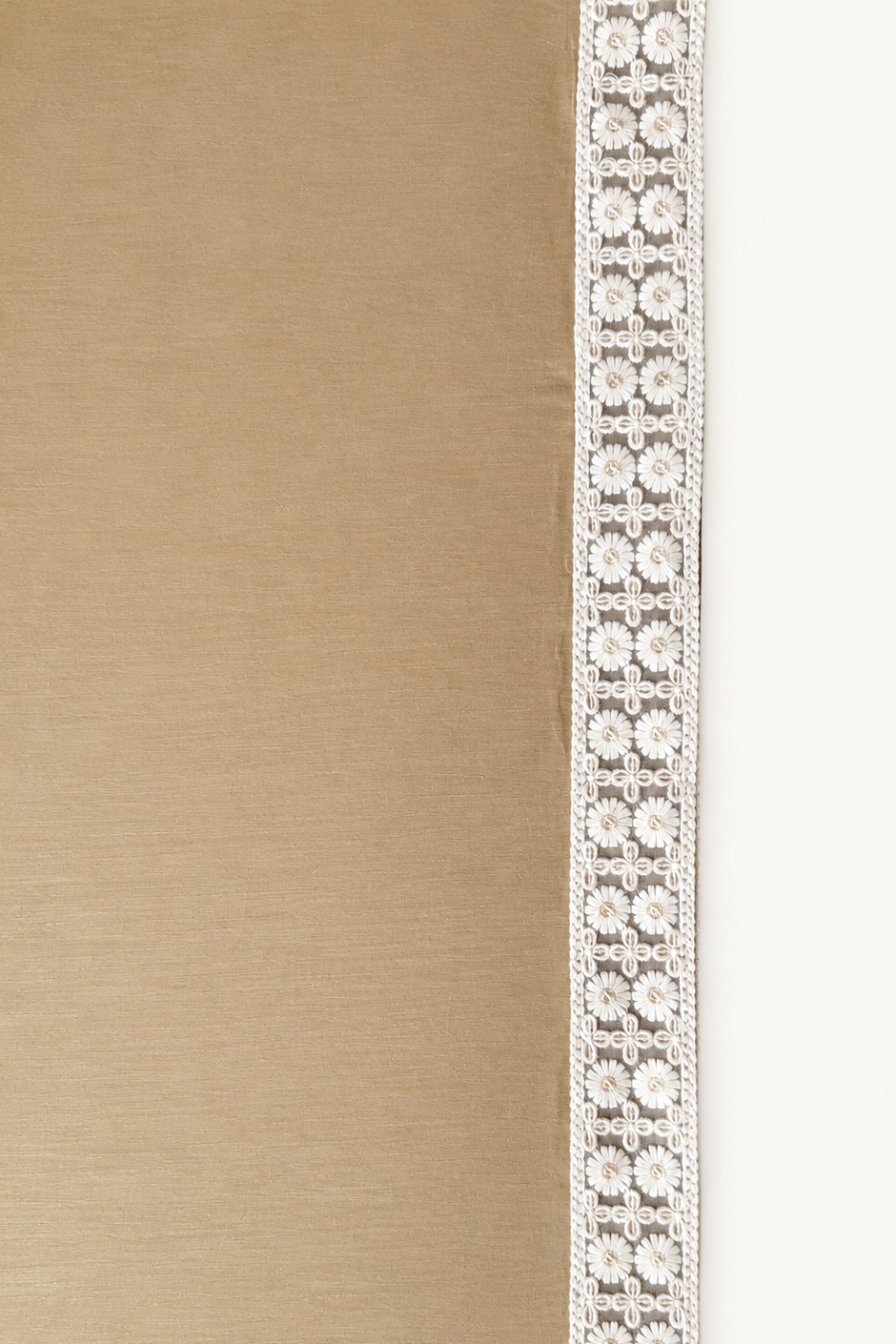 A close-up of a textured beige fabric surface with a narrow vertical white lace trim running along the left side.