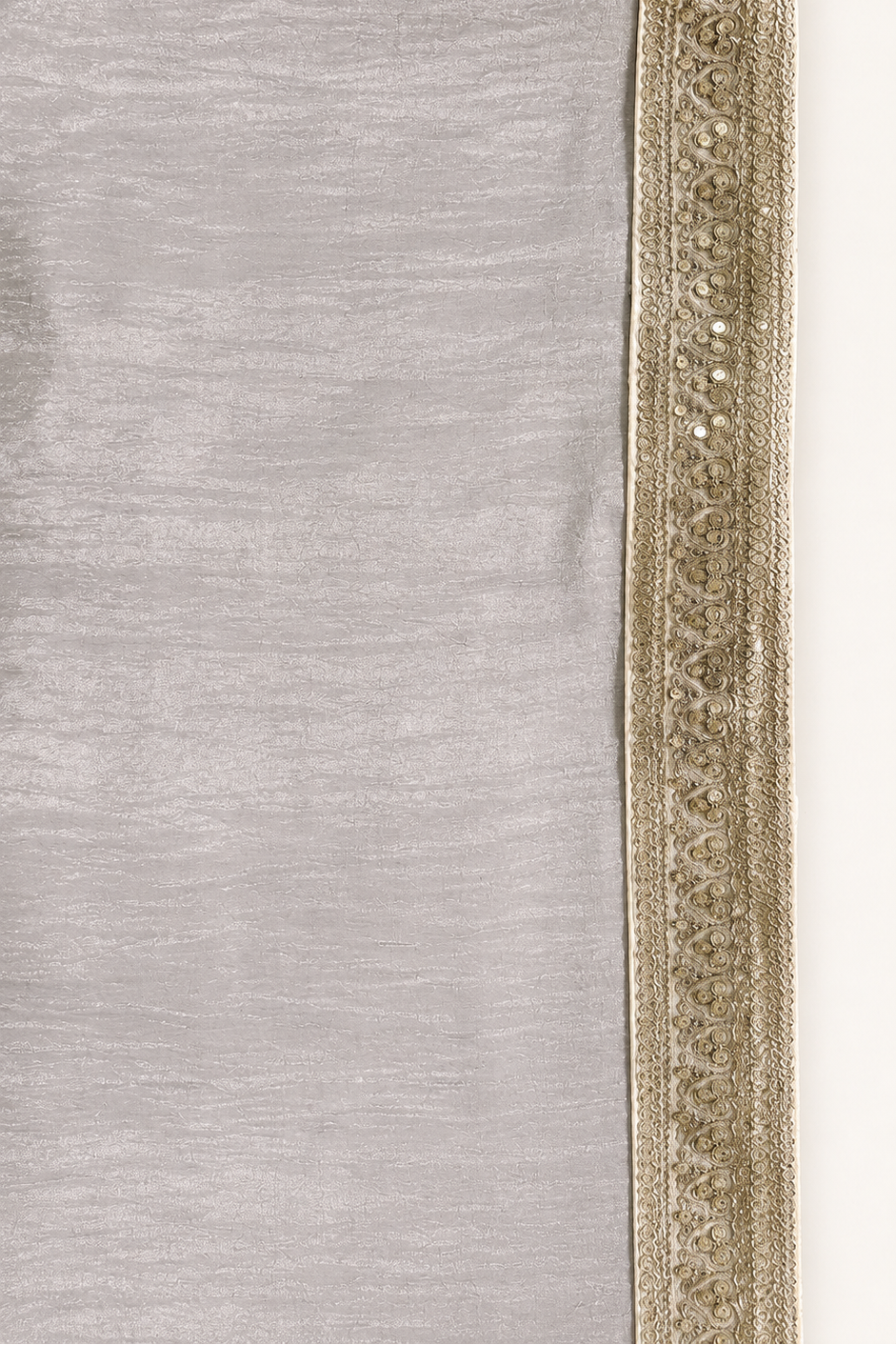 A close-up of a light gray fabric with a wide, ornate metallic gold embroidered border along one edge.