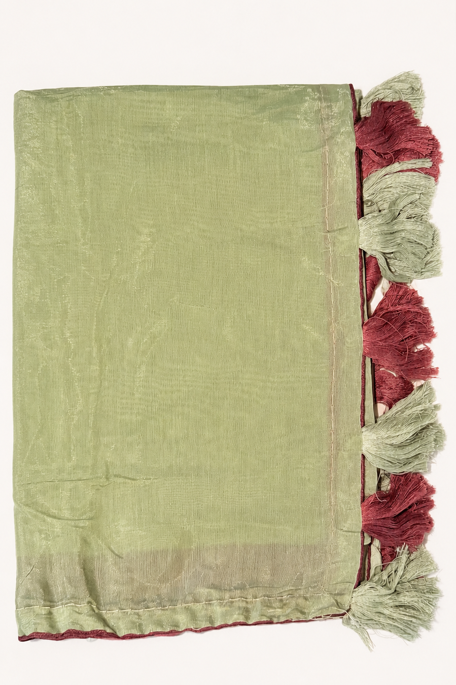 A sage green woven textile with a decorative border and tassel fringe in dusty red and light beige, laid flat against a white background.