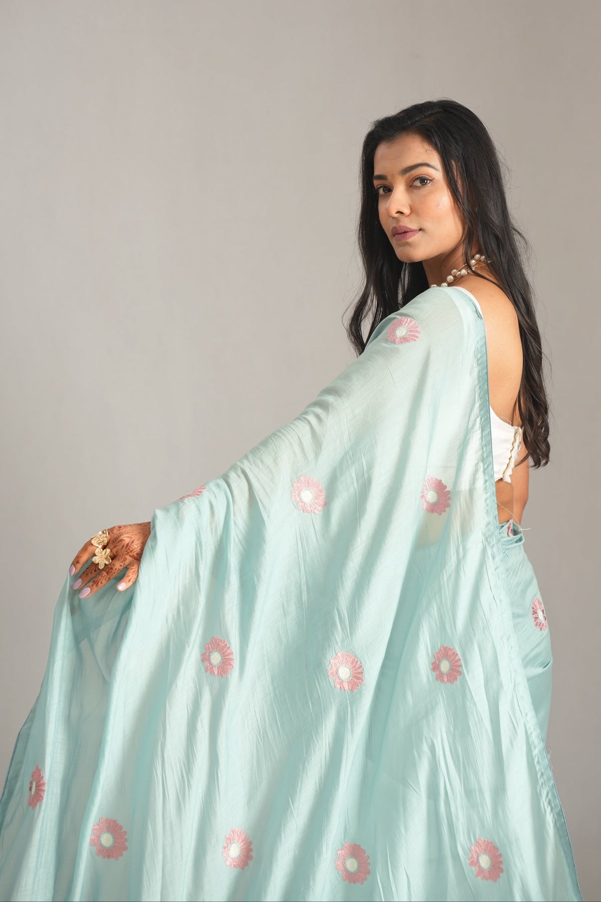 A woman wearing a light mint green saree with pink floral motifs, posing against a neutral gray studio background.
