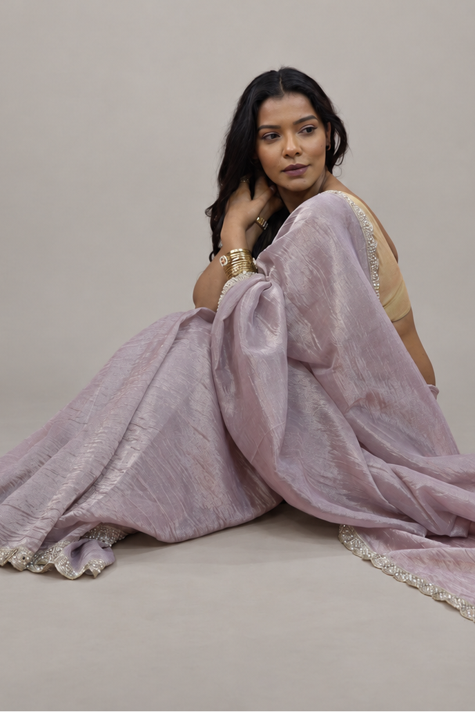 A woman wearing a lavender-purple saree with silver zari embroidery, posing on a neutral beige studio background.